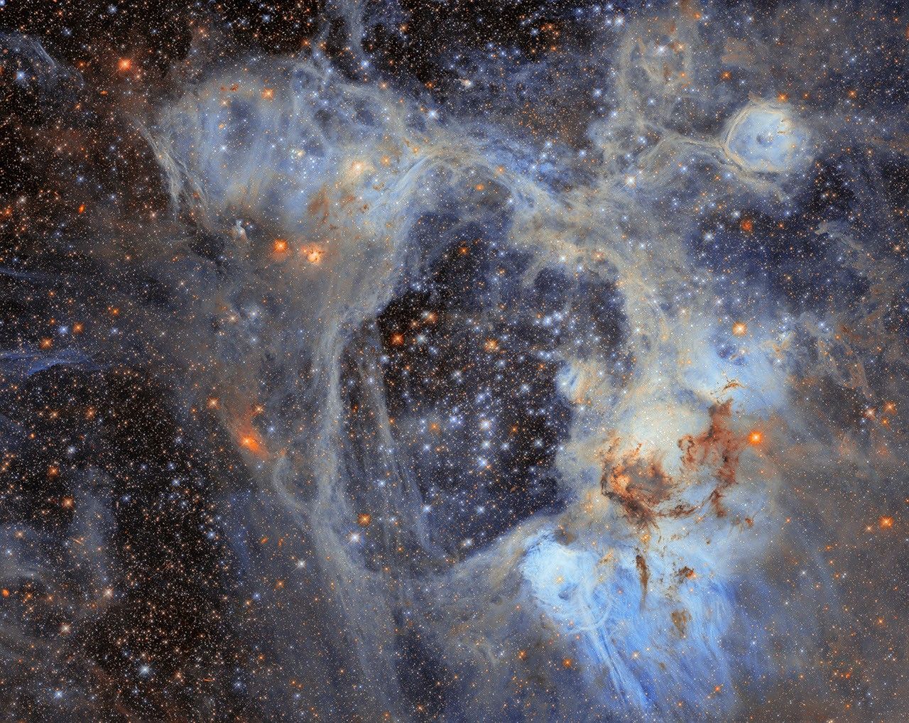 航天图片资料 · A dense field of stars fills the image, surrounded by wispy clouds of gas and dust. Pale blue and grey nebulosity forms an intricate web across the scene, with darker clouds of dust concentrated towards the lower right. Numerous bright stars appear in shades of blue, white, and orange.